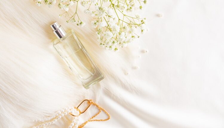 top view of a chic bottle of women’s perfume on a pastel satin fabric background with pearls and a gypsophila branch. advertising concept.